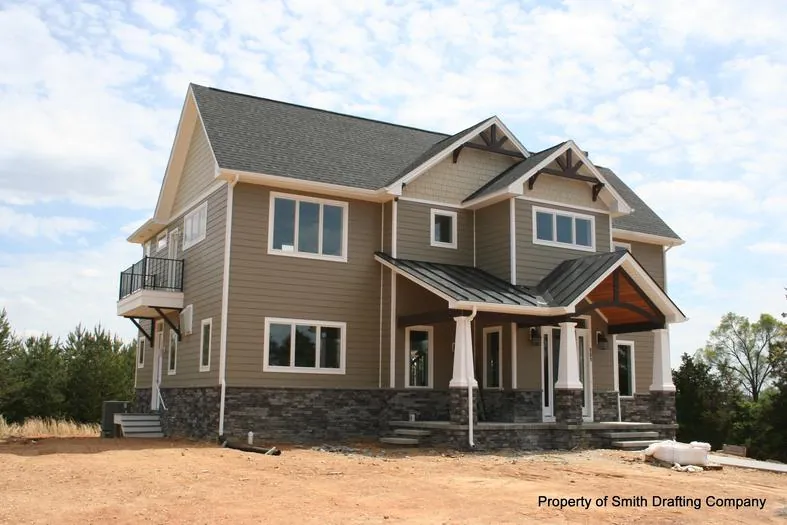 Two-story home with a covered front porch, white railings, and stone column bases.