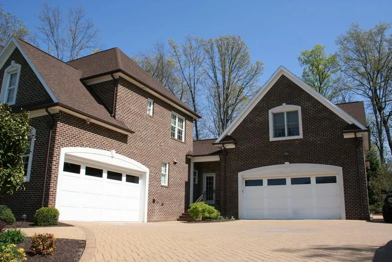 Brick home with two white garage doors and a paver driveway.