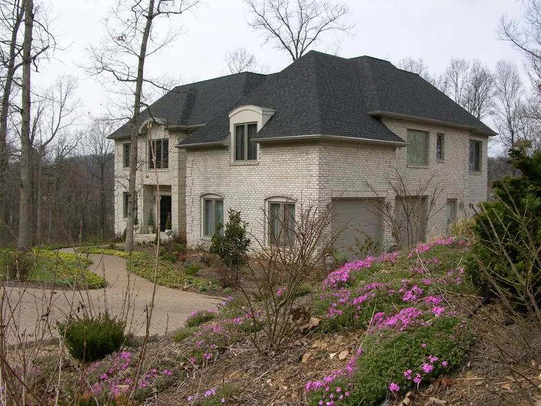 Light stucco home with a hip roof, seen past a bank of flowering plants.