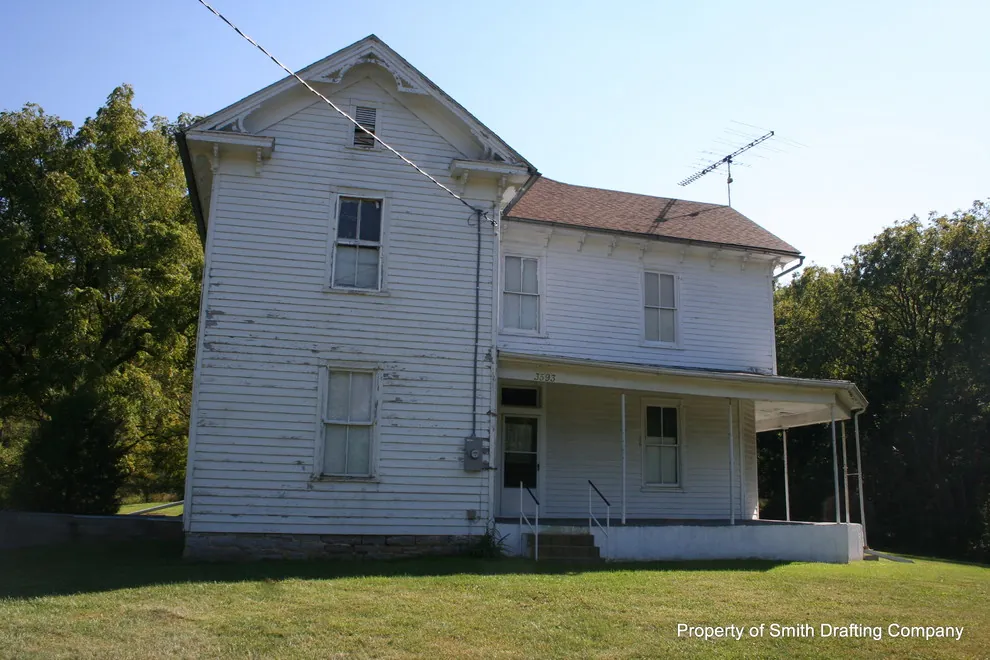 Two-story white frame farmhouse with a wraparound porch, before any work.