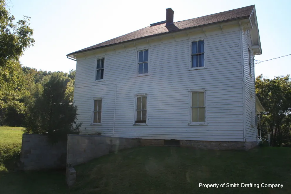 Side wall of the two-story frame farmhouse with a brick chimney at the roof.