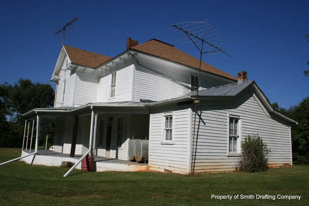 The farmhouse from another corner, showing the porch, a lower wing, and a roof antenna.