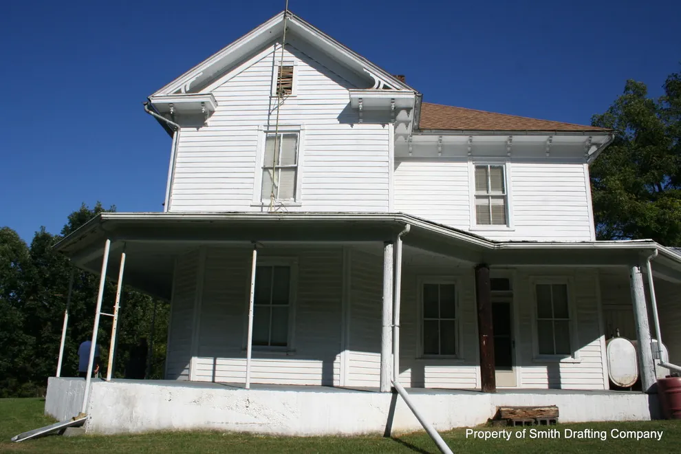 Front gable of the farmhouse above a wraparound porch with thin posts.