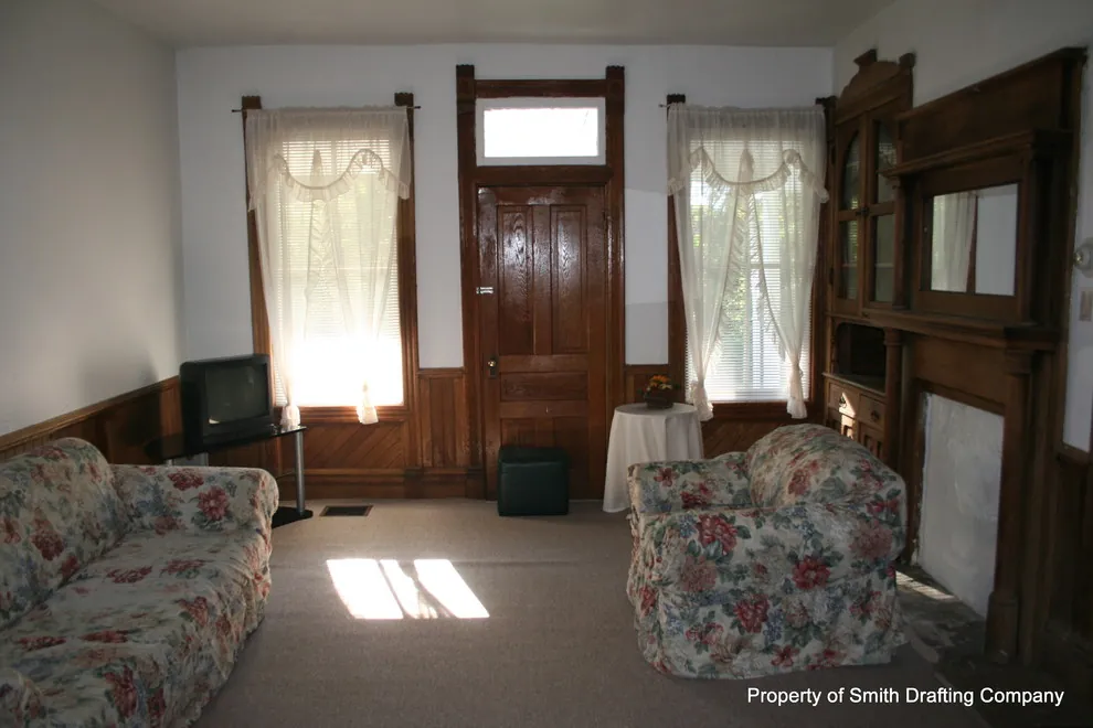 Front room with two curtained windows, a wood door with a transom, and dark wood trim.