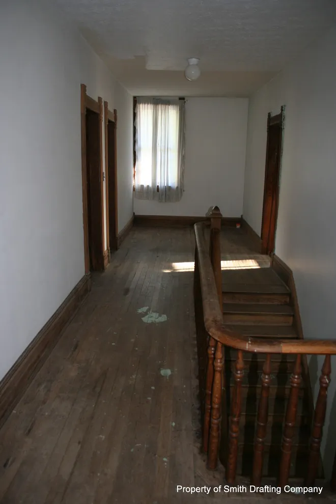 Upper hall with a turned-baluster stair railing, wood floors, and a window at the end.