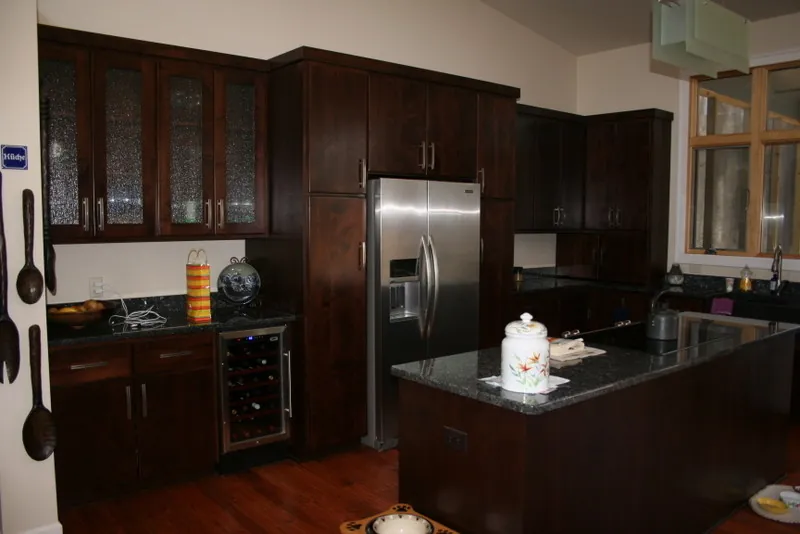 Kitchen with dark wood cabinets, glass-front uppers, and a stainless refrigerator.