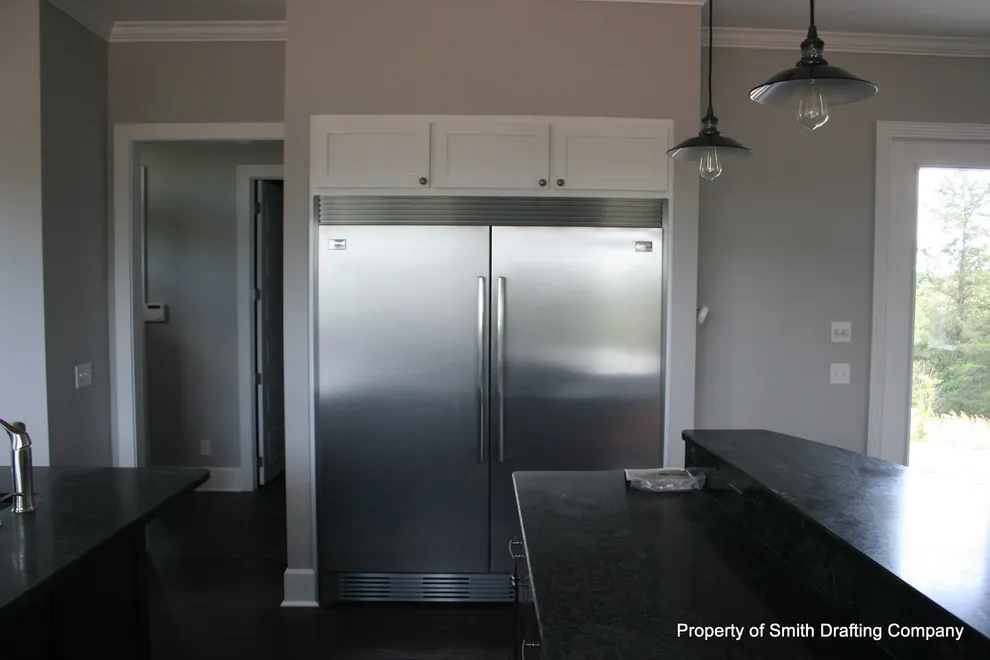 The same kitchen, showing a wide stainless refrigerator set into white cabinets.